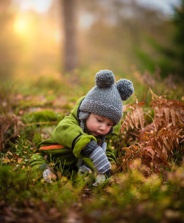 A cute baby in a knit hat and green outfit exploring nature during sunset.